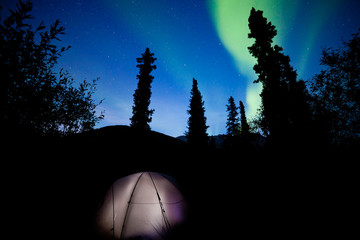 Taiga tent illuminated under northern lights flare