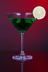 Green cocktail in martini glass on dark red background