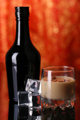 Baileys liqueur in bottle and glass on red background