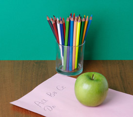 Pencils on a glasses, green apple and paper on the desk.