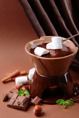 Chocolate fondue with marshmallow candies, on brown background