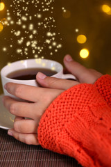 Hands holding mug of hot drink, close-up, on bright background