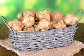 Topinambur roots in wicker basket on table on bright background