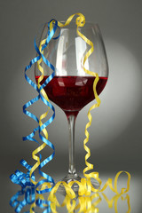 Fototapeta na wymiar Glass of red wine and streamer after party on gray background