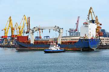 Fototapeta premium Tugboat assisting bulk cargo ship to harbor quayside