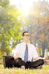 Fototapeta premium Young businessperson seated on grass meditating on a sunny day