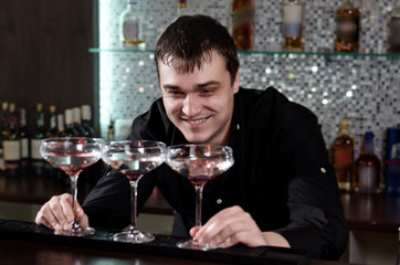 Barman grinning as he plays with three cocktails