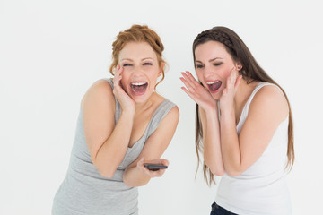 Fototapeta na wymiar Shocked cheerful female friends with mobile phone