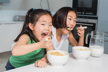 Two smiling young girls eating cereals in kitchen
