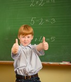 Little funny redhead schoolboy near blackboard with thumbs up