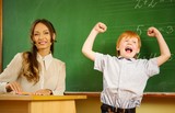 Little happy redhead boy answering near blackboard in school