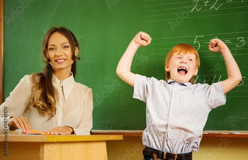 Little happy redhead boy answering near blackboard in school