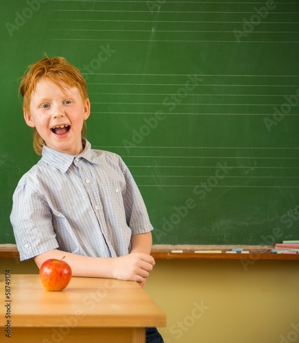 Little funny redhead schoolboy near blackboard 