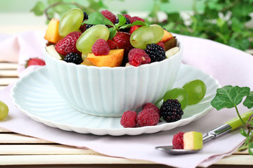 Fruit salad in bowl, on wooden table, on bright background
