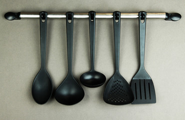 Plastic kitchen utensils on silver hooks on grey background