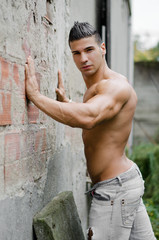 Muscular young latino man shirtless in jeans against wall