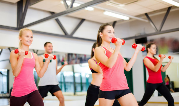 group of smiling people working out with dumbbells