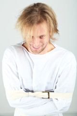 Mentally ill man in strait-jacket on gray background