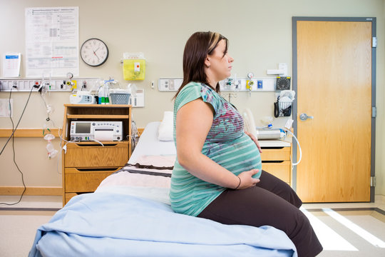 Pregnant Woman With Hands On Stomach On Hospital Bed