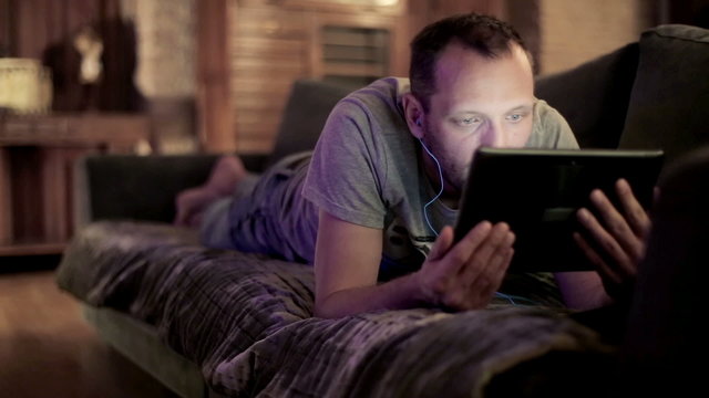 Young Man Watching Movie On Tablet Computer On Sofa