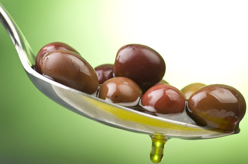Spoon with black olives and oil on a green background