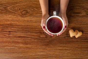woman holding hot cup of tea with cookies on wooden table