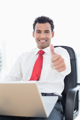 Smiling businessman with laptop gesturing thumbs up