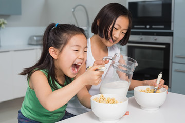 Two happy young girls eating cereals in kitchen