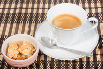 a cup of coffee with almond cookie on bamboo mat