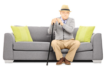 Thoughtful senior man with a cane sitting on a sofa