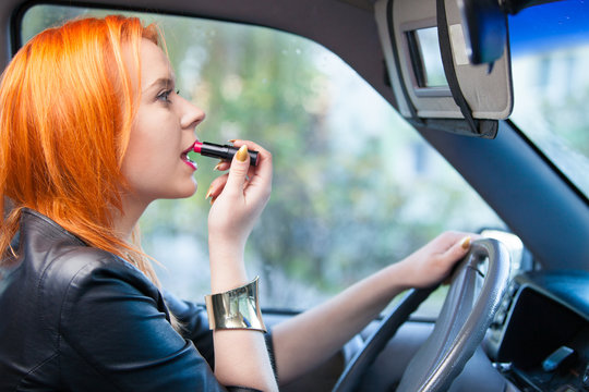 Woman driver painting her lips while driving a car