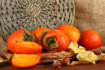 Ripe persimmons with nuts on table on wicker background
