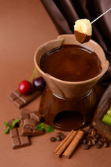 Chocolate fondue with fruits, on  brown background