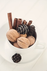 Cup with walnuts, cinnamon sticks and fir-cones, high angle view