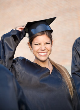 Woman In Graduation Gown Holding Mortar Board On Campus