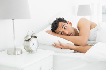 Obraz na płótnie Canvas Sleepy man looking at the alarm clock in bed