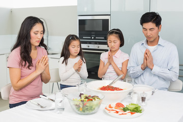 Family of four saying grace before meal in kitchen