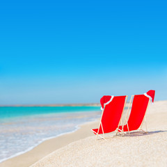 Santa hat on chaise longues at white sand beach against the sea