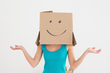 Woman in blue tank top with smiley cardboard box over face