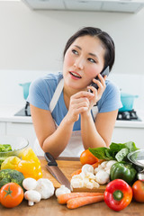 Woman using mobile phone in front of vegetables in kitchen