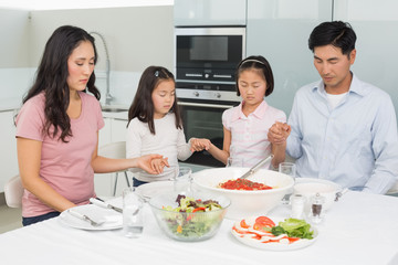 Family of four saying grace before meal in kitchen