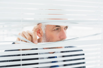 Close-up of a businessman peeking through blinds in office