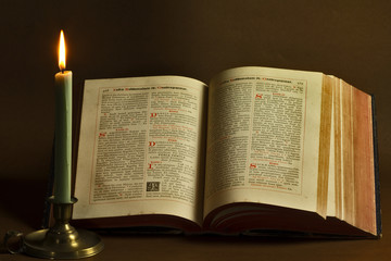 Opened old book and candle - obrazy, fototapety, plakaty