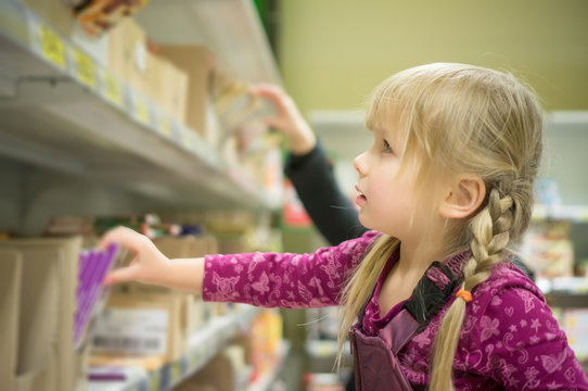 Adorable girl select chocolate bars on shelf in supermarket