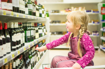 Adorable girl grimacing sitting in shopping cart in alcoholic be