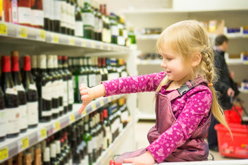 Adorable girl grimacing sitting in shopping cart in alcoholic be