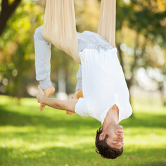 Aerial yoga, man doing yoga exercises in the park