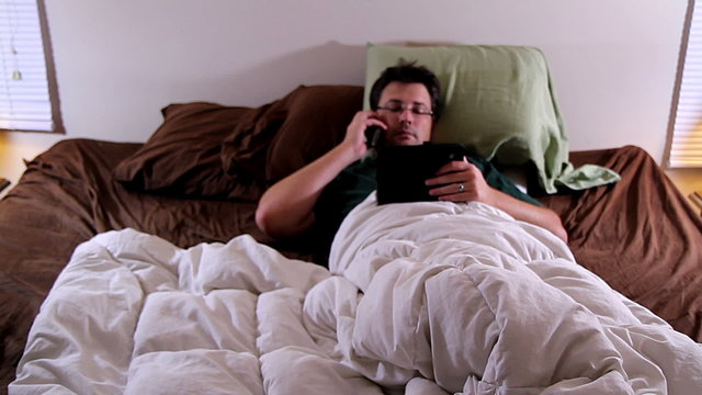 Man in bed on phone and on tablet, multitasking