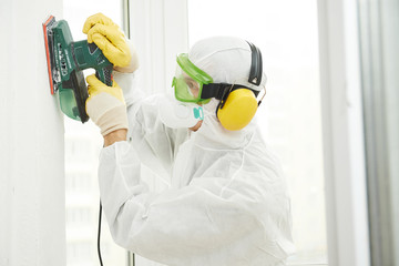 worker with sander at wall filling