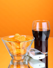 Chips in bowl, cola and TV remote on orange background